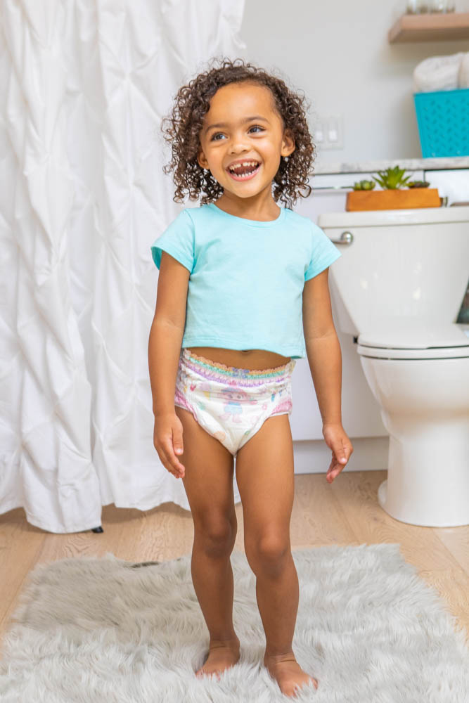 A toddler girl dancing in the bathroom wearing her pamper diaper. 