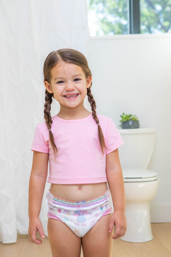 A toddler girl standing bathroom wearing her pamper diaper. 